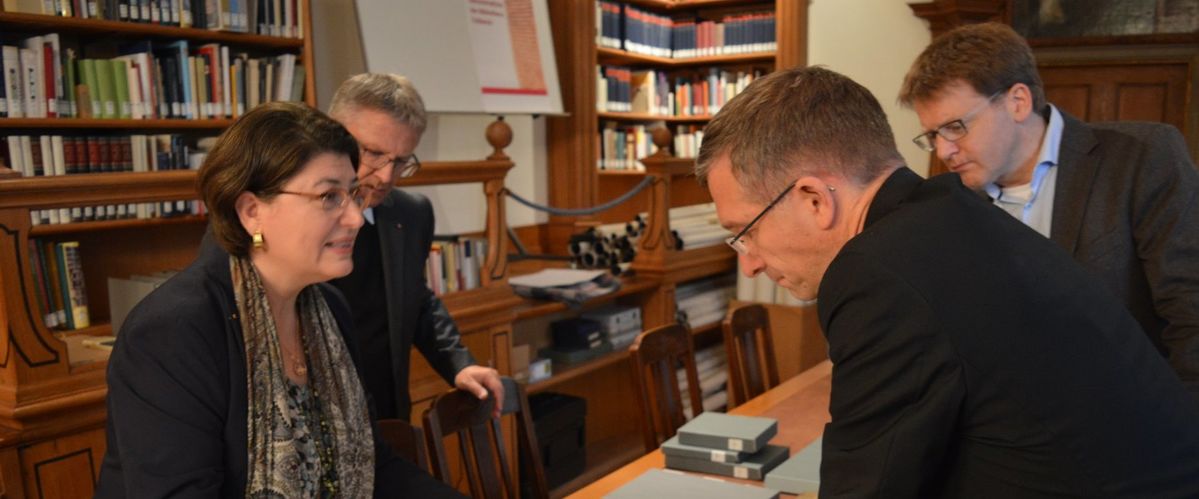 Dr. Sorbello Staub zeigt dem Bischof ein Handschriftenfragment aus dem 8. Jahrhundert; im Hintergrund links Rektor Müller und rechts persönlicher Referent Zürcher.